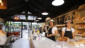 Ein Café-Interieur mit Theke, auf der Gebäckstücke ausgestellt sind, einer Speisekarte und einem Sitzbereich mit Stühlen und Tischen.