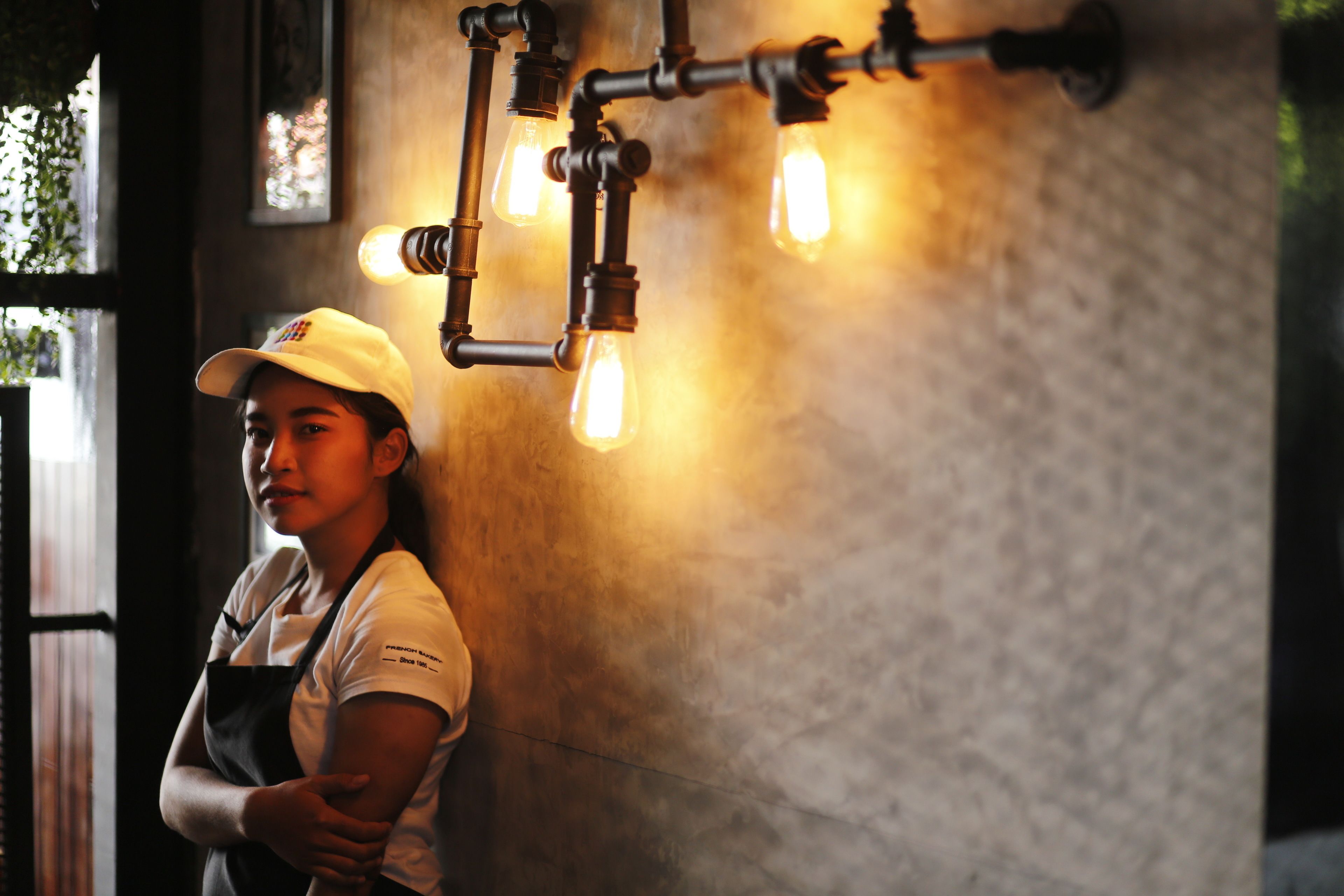A person standing in a room with a rustic industrial light fixture on the wall.