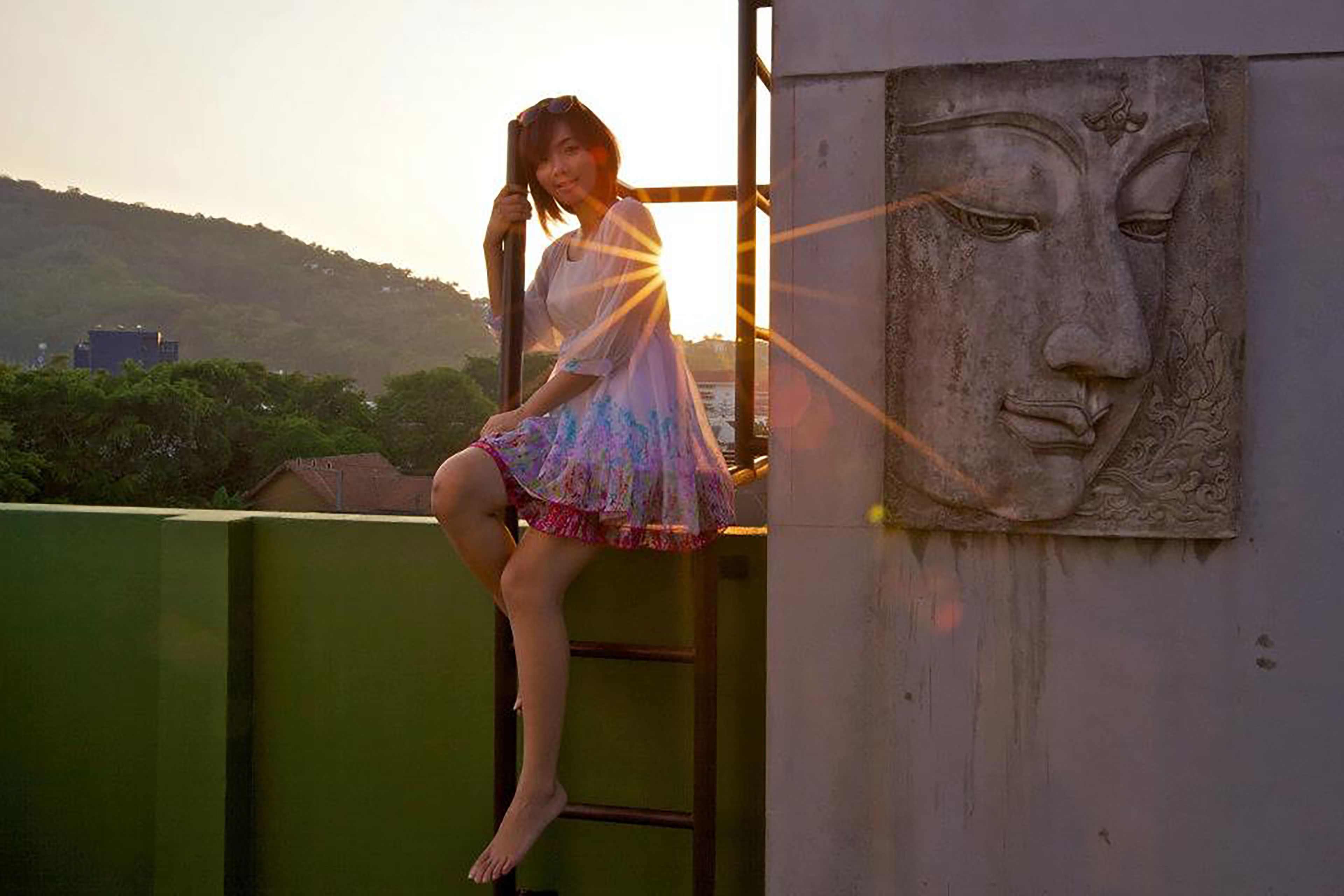A person sitting on a ladder next to a wall with a carved face.