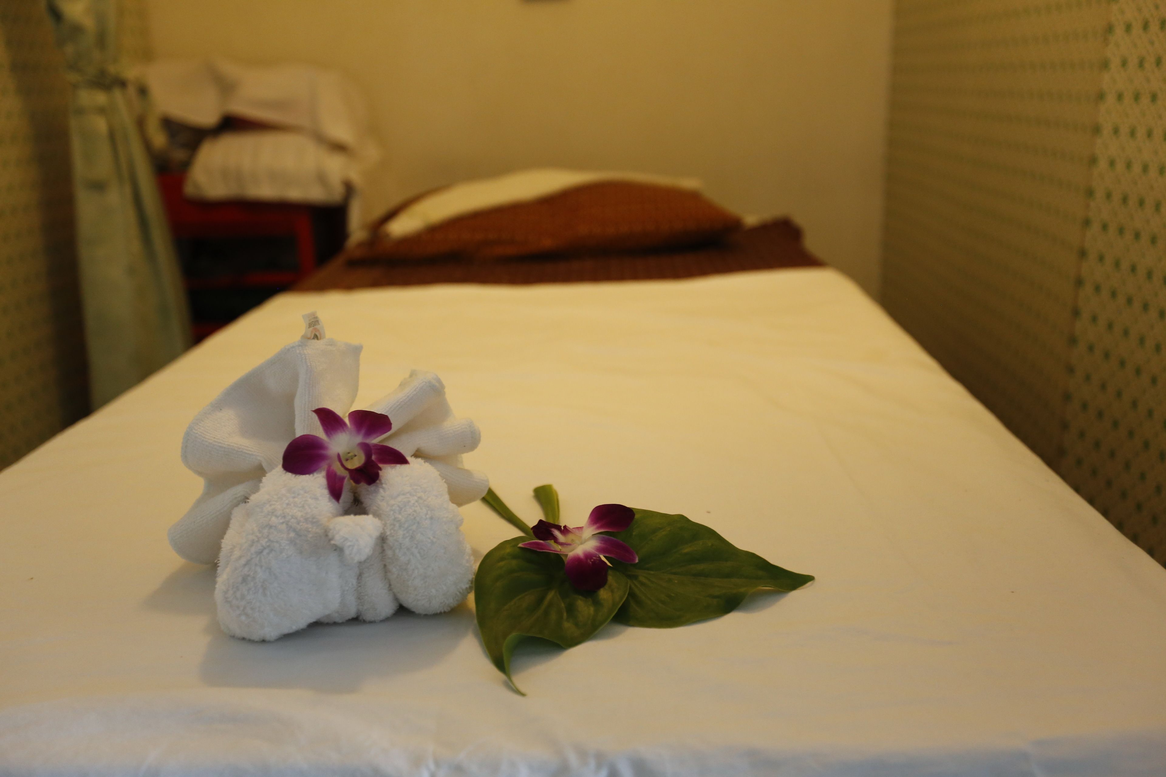 A neatly made bed with a towel and an orchid.