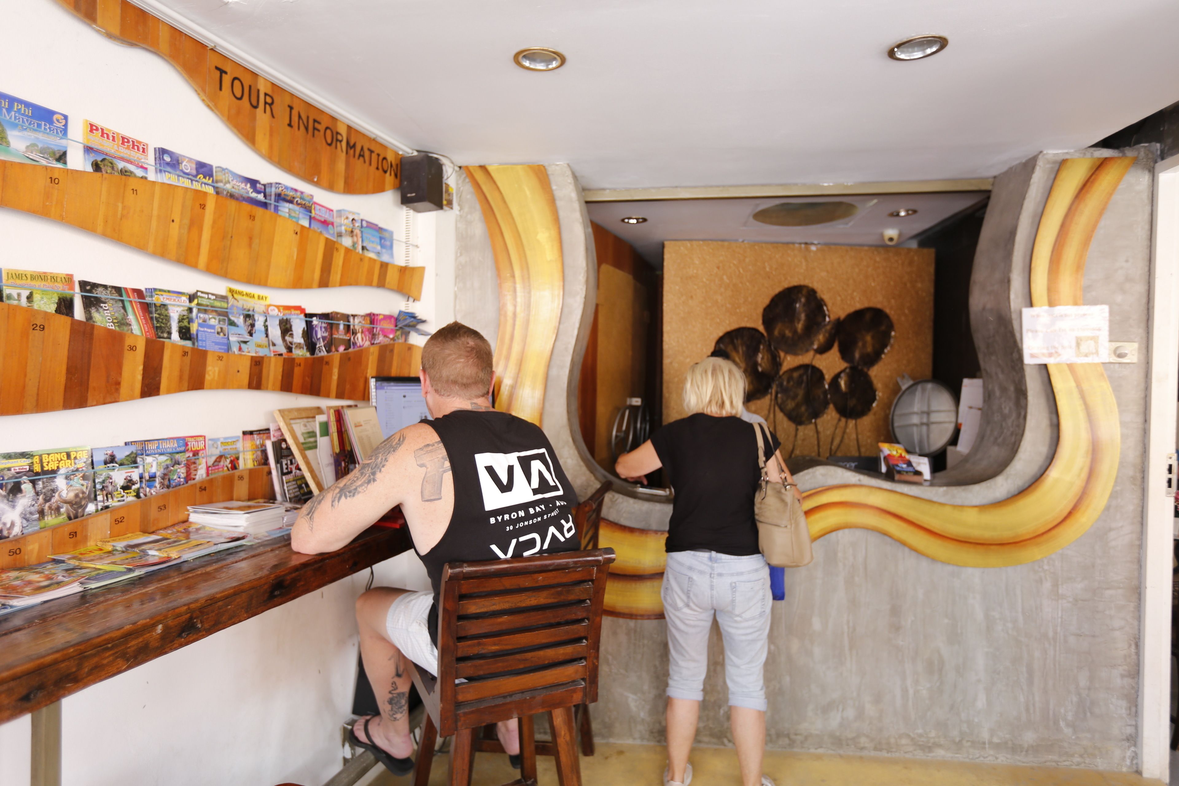 A reception desk with a wooden panel wall displaying various travel brochures.