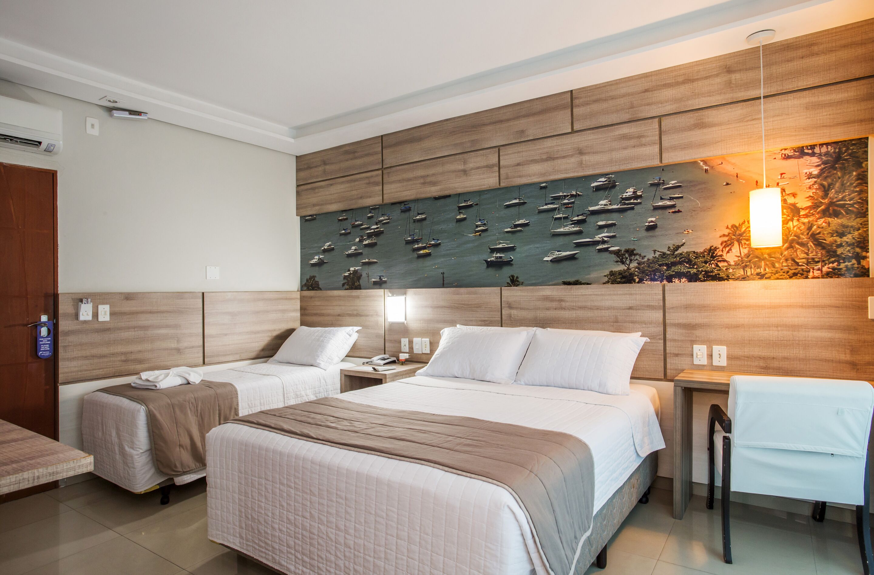 Habitación de hotel con dos camas, cabecera de madera, un mural en la pared con barcos, un escritorio y una silla.