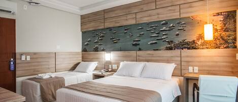 Habitación de hotel con dos camas, cabecera de madera, un mural en la pared con barcos, un escritorio y una silla.