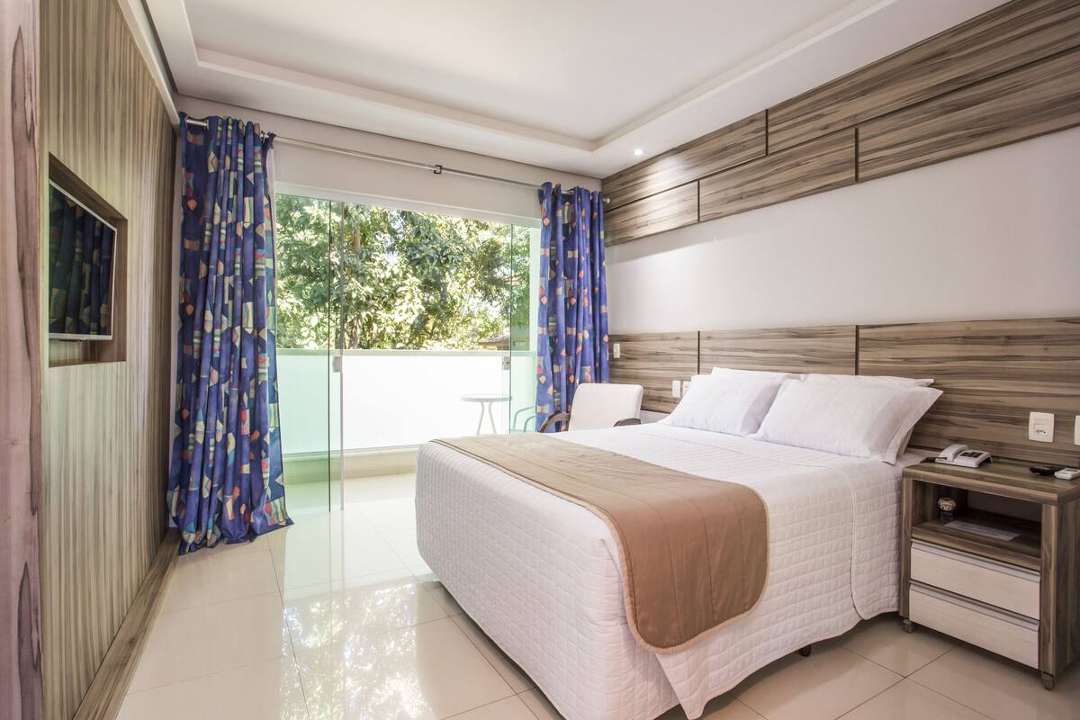 Una habitación de hotel moderna con una cama grande, cabecera de madera, mesita de noche y vista a zonas verdes.