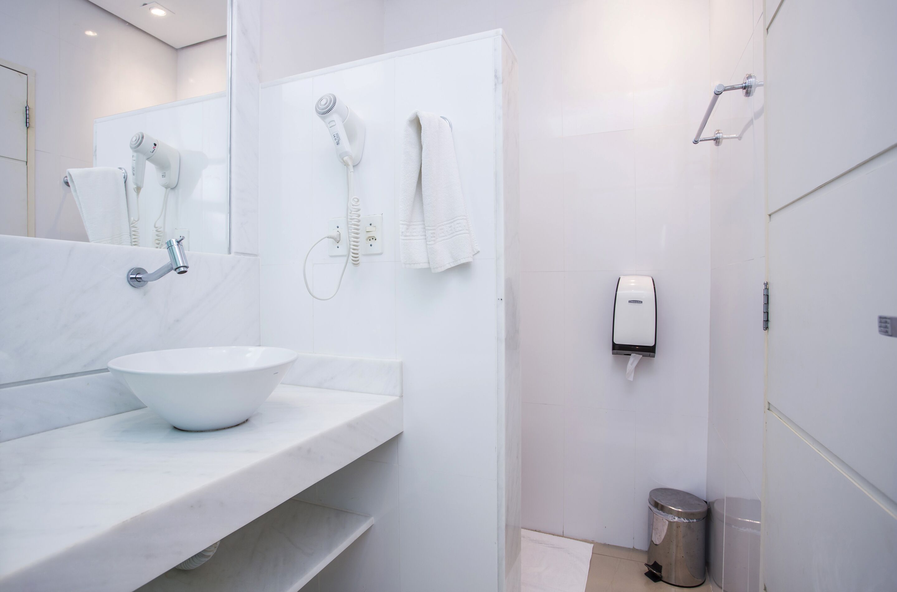 A modern bathroom with a white sink, towel rack, hairdryer, and a trash bin.