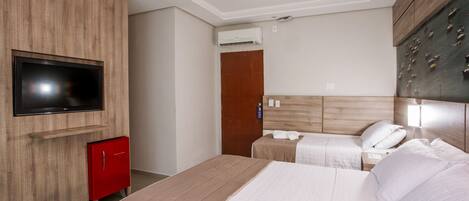 Una habitación de hotel con una cama grande, un televisor montado en la pared, un minibar rojo y un cabecero de madera.