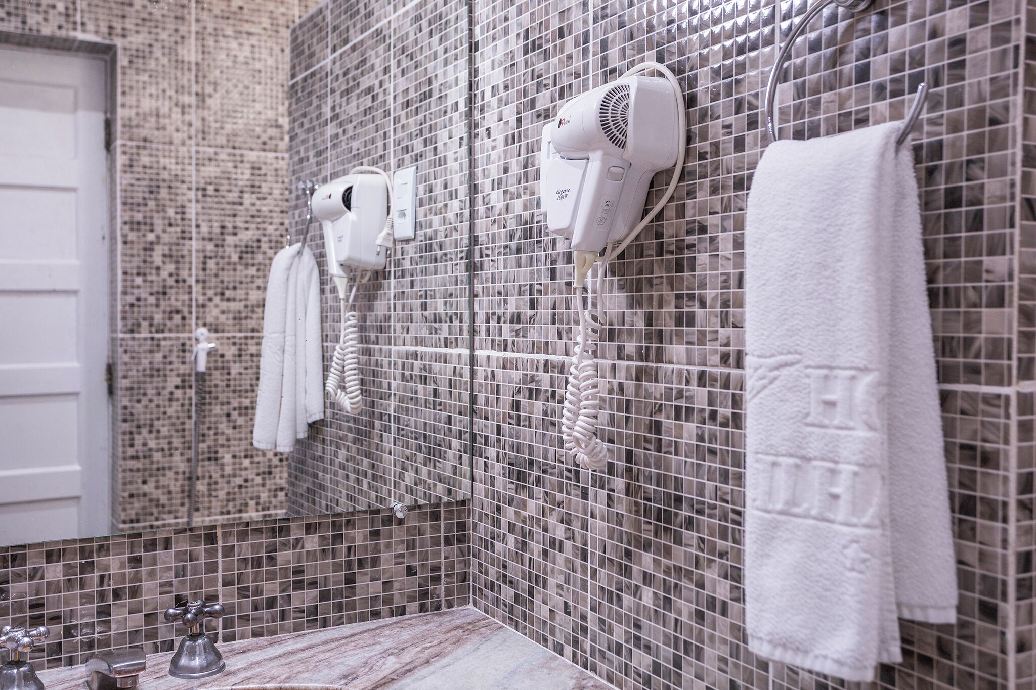 A bathroom with a tiled wall, a white towel hanging on a rack, and a hairdryer mounted on the wall.