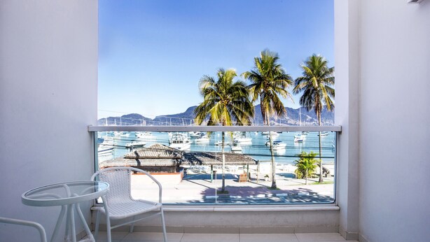 Een balkon met witte rieten meubels, uitzicht op een jachthaven met boten en palmbomen.