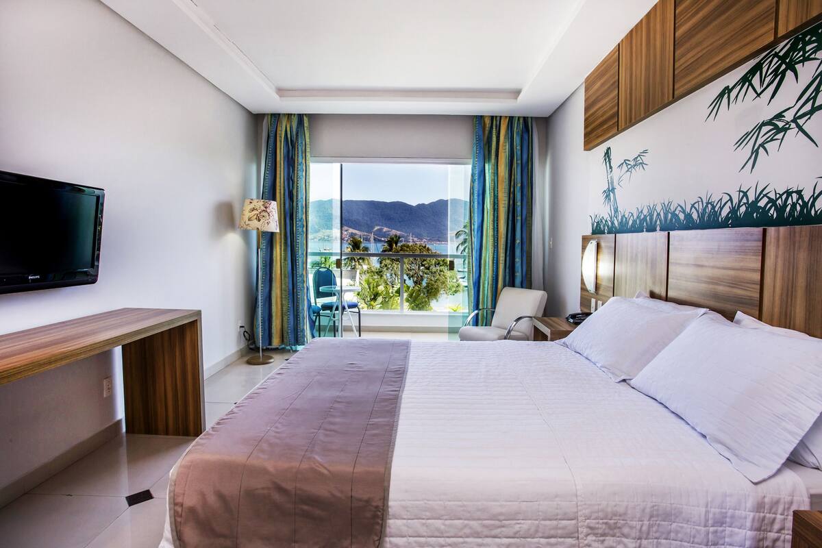Habitación de hotel con una cama grande, un televisor en la pared, un escritorio y vistas a la montaña por la ventana.