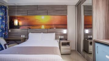 Quarto de hotel com uma cama grande, mesa de cabeceira, escrivaninha, espelho e guarda-roupa.