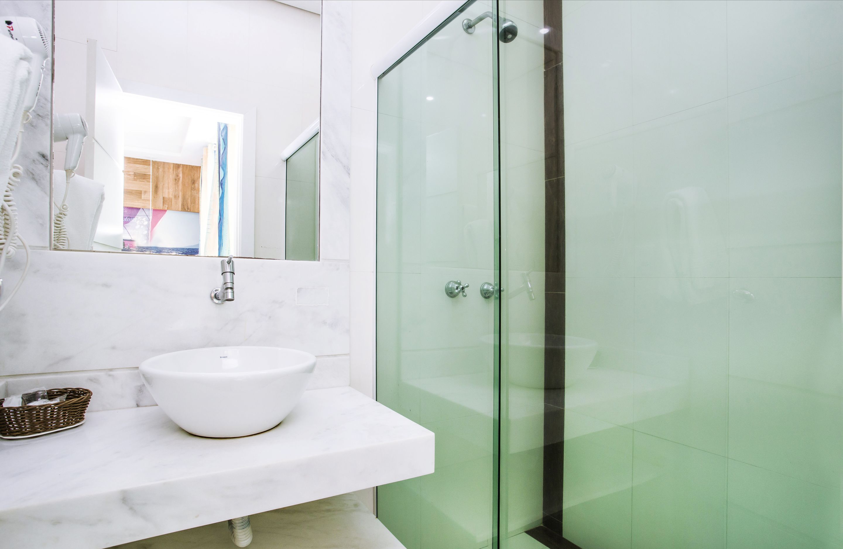 Een badkamer met een wit marmeren wastafel, een douche met glazen wanden en een spiegel die een houten deur weerspiegelt.