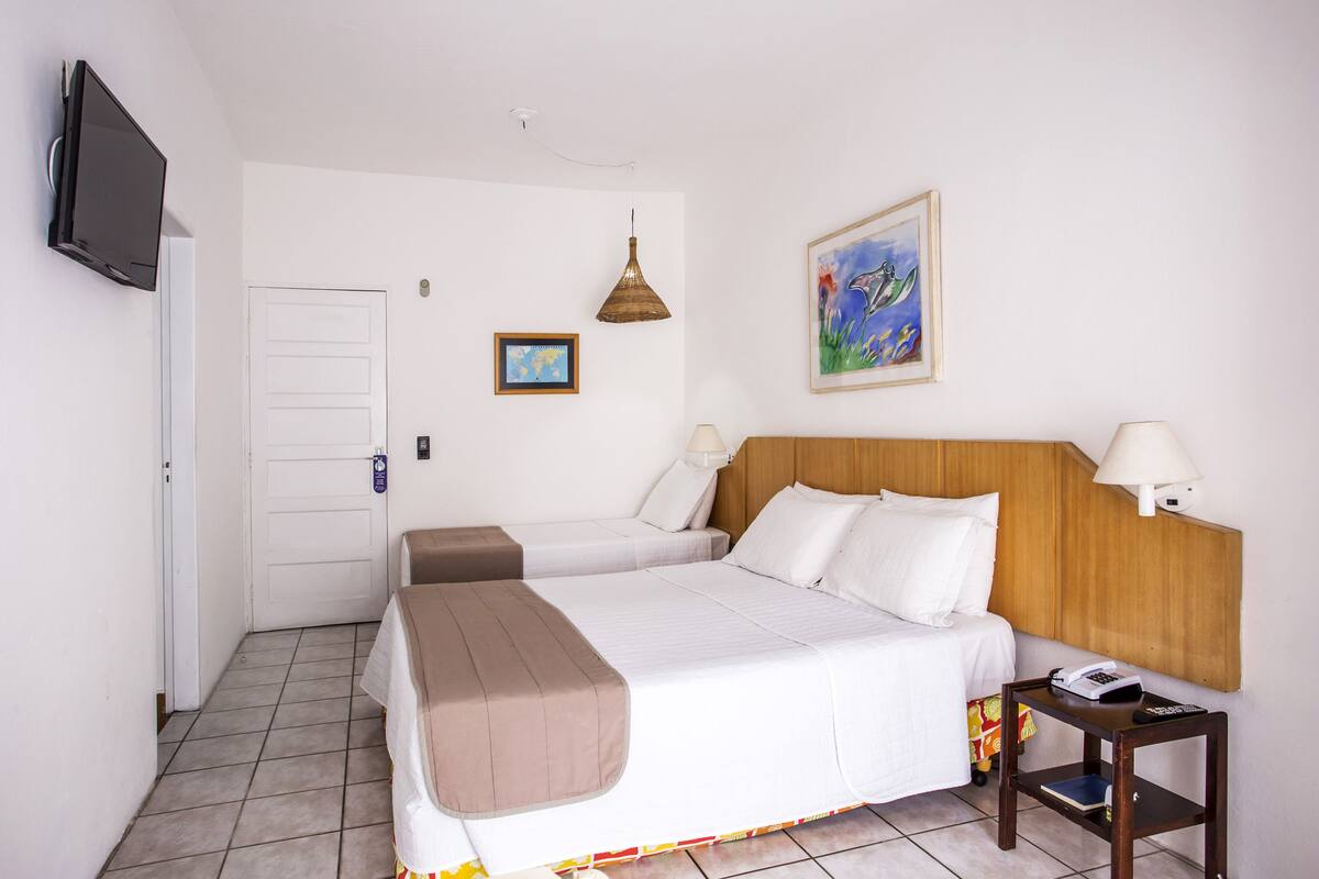 Una habitación de hotel con dos camas, televisión, lámpara, un cuadro y una mesita con teléfono.