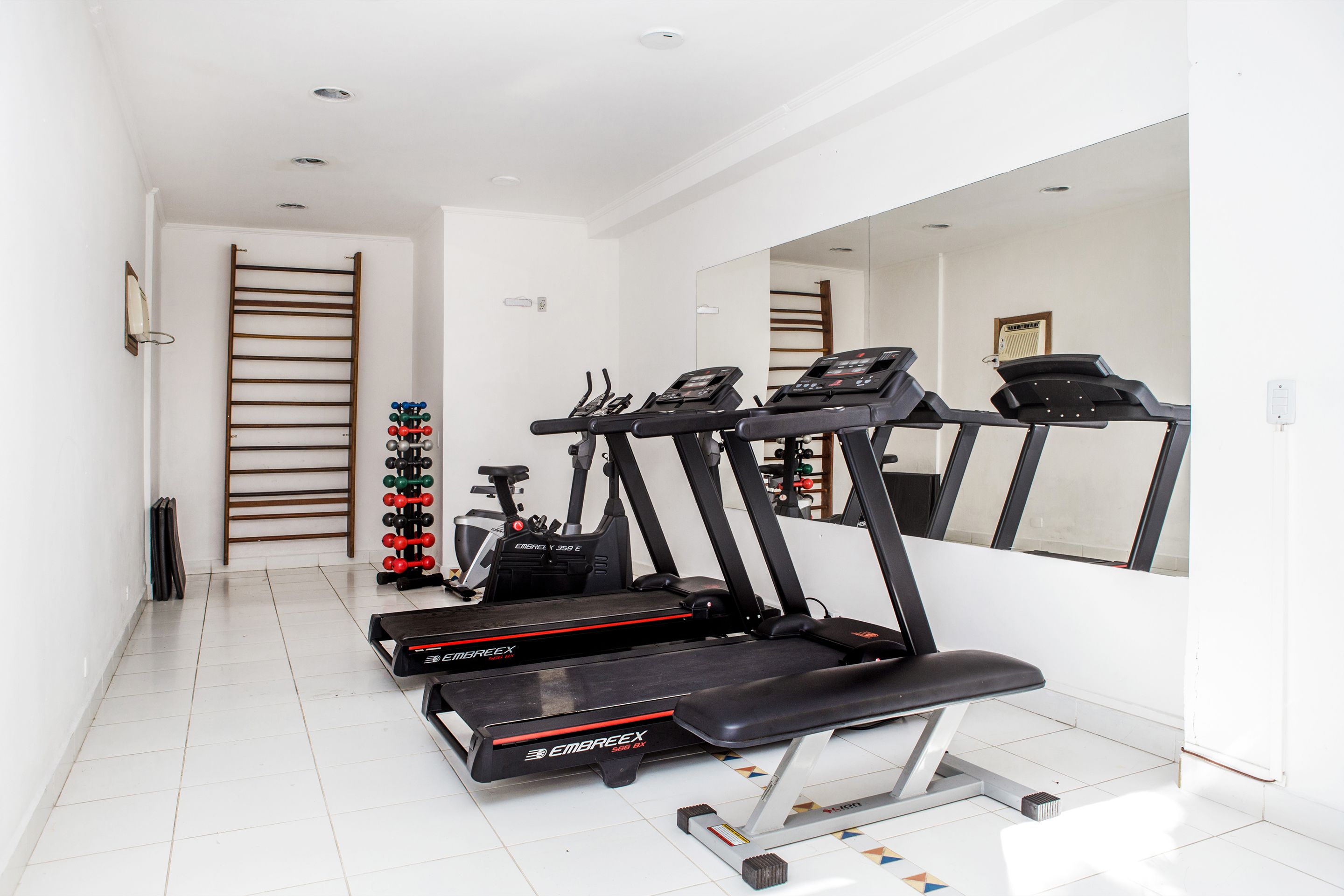 A gym with treadmills, a bench, and a mirror.