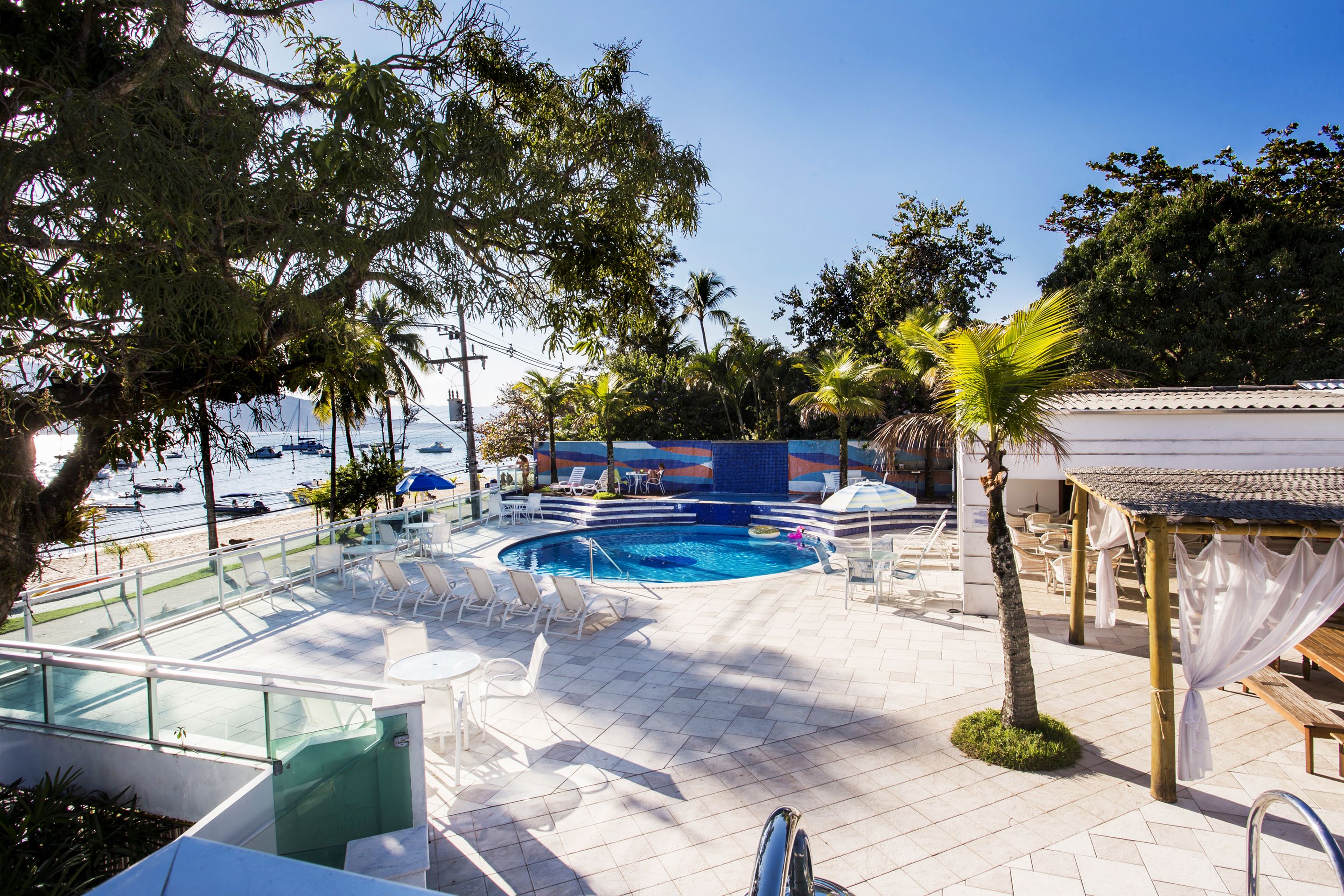 A pool area with lounge chairs, a small pool, and a view of the sea with boats.