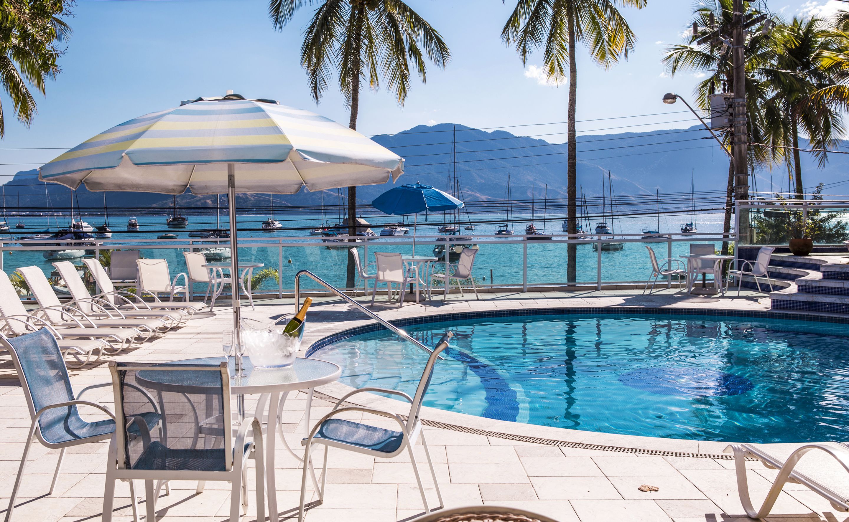 A pool area with lounge chairs, umbrellas, and a view of the sea and mountains.