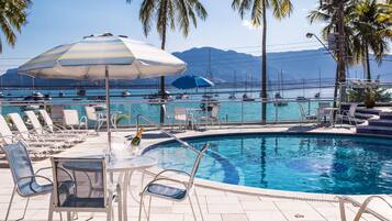 A pool area with lounge chairs, umbrellas, and a view of the sea and mountains.