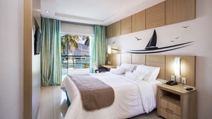 Een hotelkamer met een groot bed, een bureau, een stoel, een nachtkastje en uitzicht op zee door een raam.