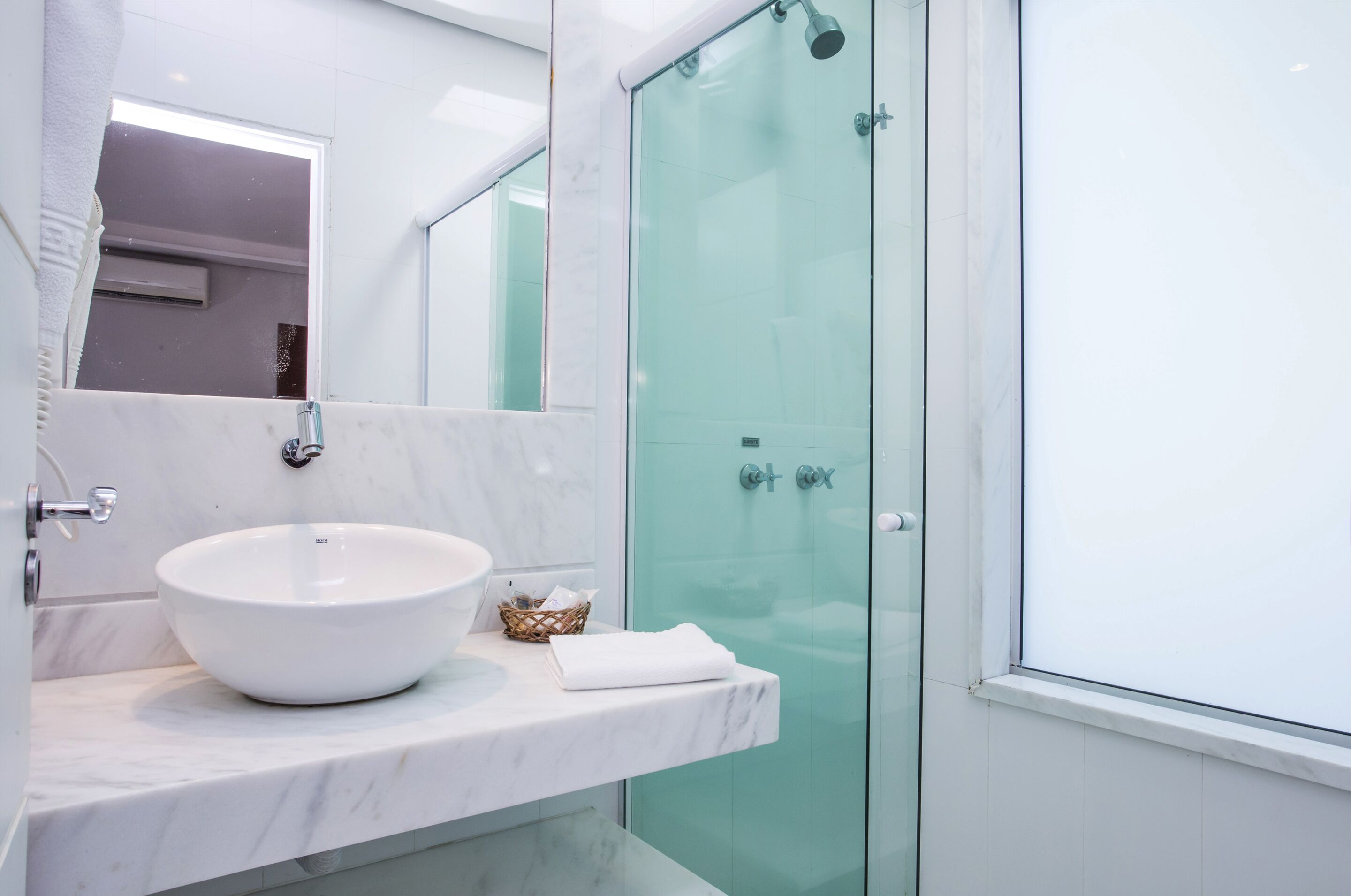 A modern bathroom with a white marble sink, a glass shower enclosure, and a large mirror.