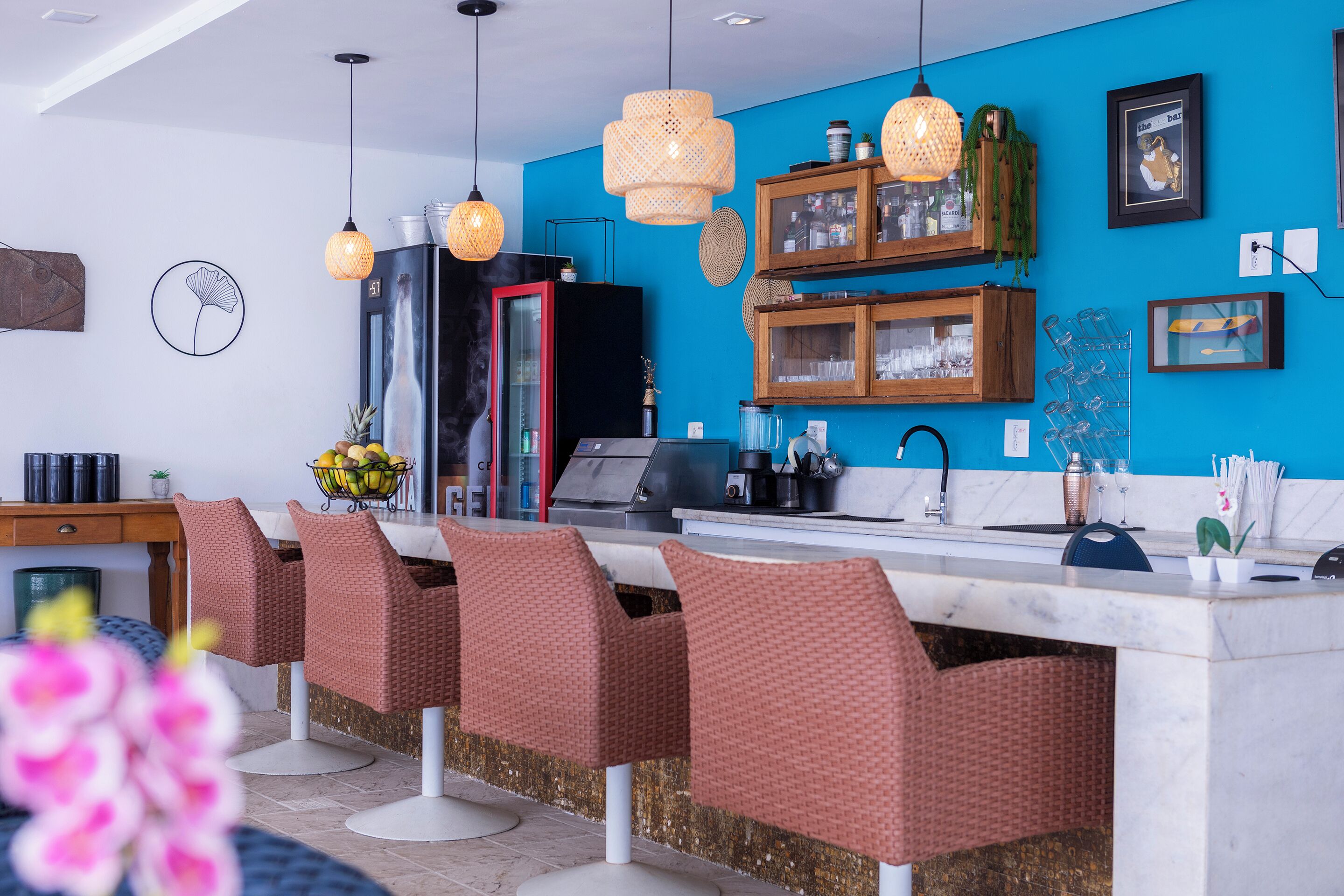 Una cocina moderna con barra, con sillas de mimbre, luces colgantes y una pared azul de acento.