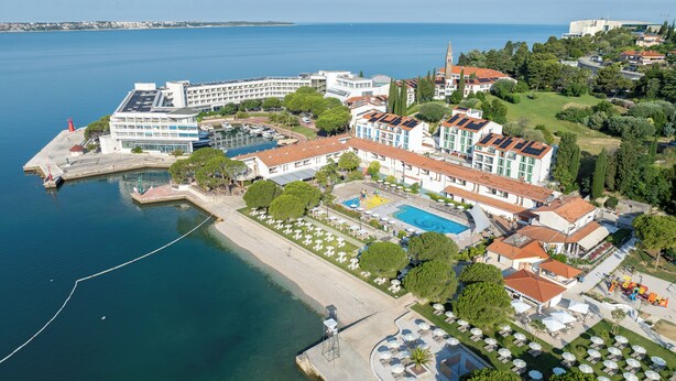 Vista aérea de un hotel costero con piscina, varias edificaciones y un puerto deportivo.