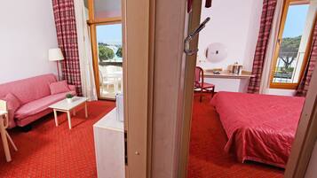 Ein Hotelzimmer mit rotem Teppich, einem rosafarbenen Sofa, einem Bett, einem Schreibtisch und einem Fenster mit Blick.