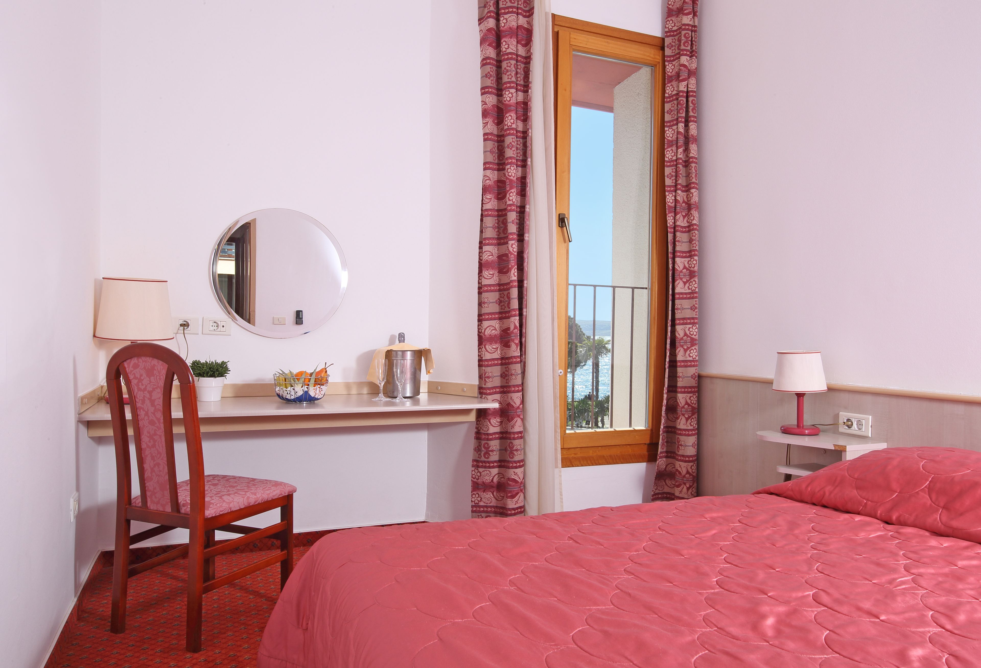 A bedroom with a bed, a desk, a chair, a mirror, and a window with curtains.