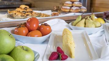 A buffet with various fruits, pastries, and a plate of scrambled eggs.