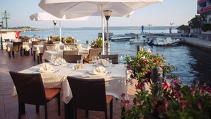 Un restaurante frente al agua con mesas dispuestas para comer, con vistas a un canal y barcos.