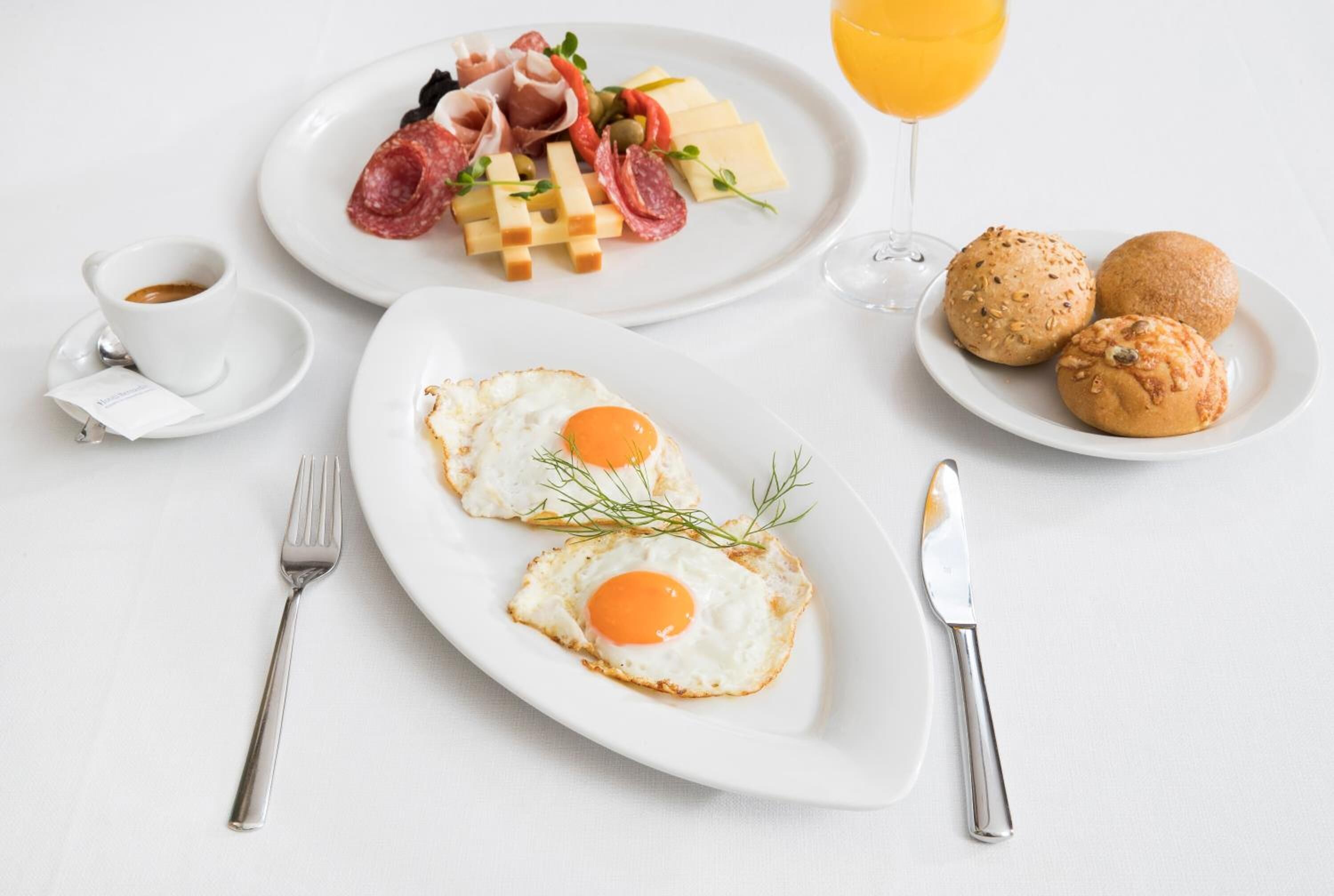 Ein Frühstückstisch mit zwei Eierplatten, einer Platte mit Fleisch und Käse sowie einem Glas Orangensaft.