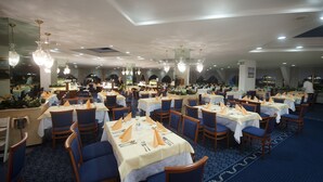 Un comedor amplio con varias mesas, sillas y candelabros de cristal colgantes.