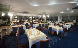 Un comedor amplio con varias mesas, sillas y candelabros de cristal colgantes.