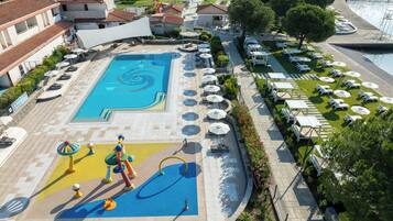 A swimming pool with a spiral design, surrounded by lounge chairs and umbrellas, with a view of the sea and buildings in the background.