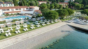 Vista aérea de un resort con piscina, tumbonas y playa de guijarros.
