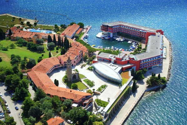 An aerial view of a coastal hotel with a swimming pool, a large building with a red facade, and a marina with boats. - Vila Barka - Sava Hotels & Resorts (Piran)