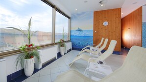 Una habitación iluminada por el sol con un ventanal grande, una pared de madera con un reloj y varios sillones.