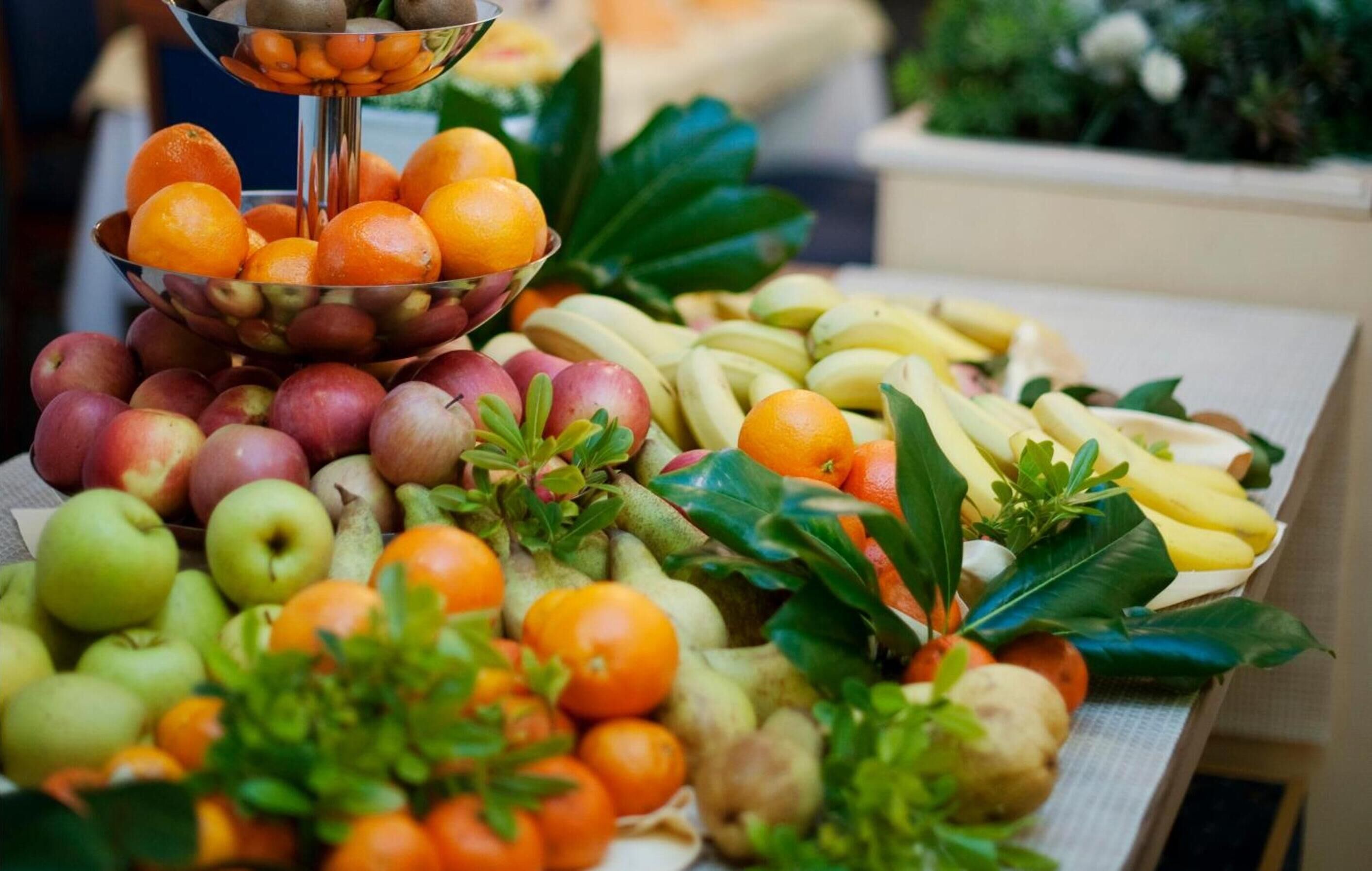 Un tavolo con diversi tipi di frutta e verdura, tra cui mele, arance, banane e verdure a foglia.