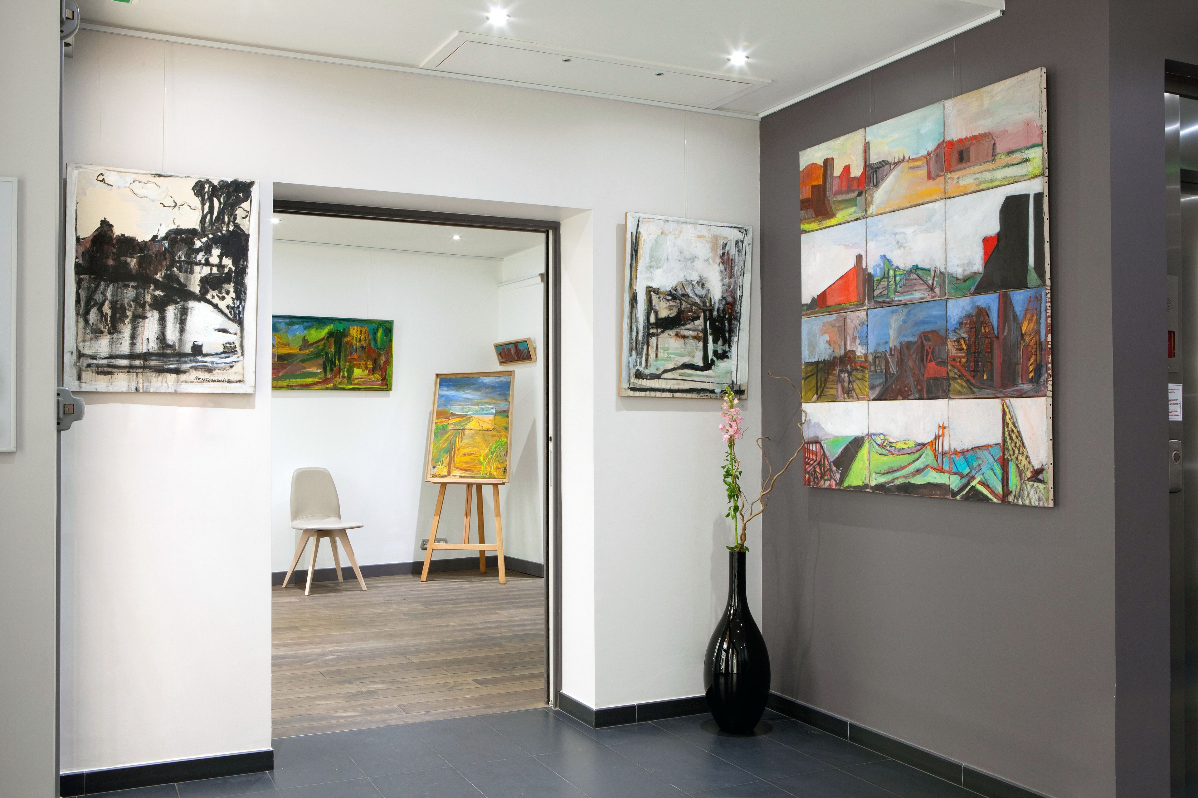 Eine Kunstgalerie mit Gemälden an den Wänden und einem Staffelei im Hintergrund.
