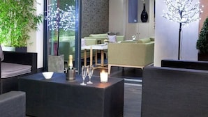 A modern lounge area with seating, a table with a bottle and glasses, and a decorative tree. - Serotel Suites (Paris)