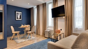A modern hotel room with a dining area, a sofa, a TV, and a window with curtains. - Serotel Suites (Paris)