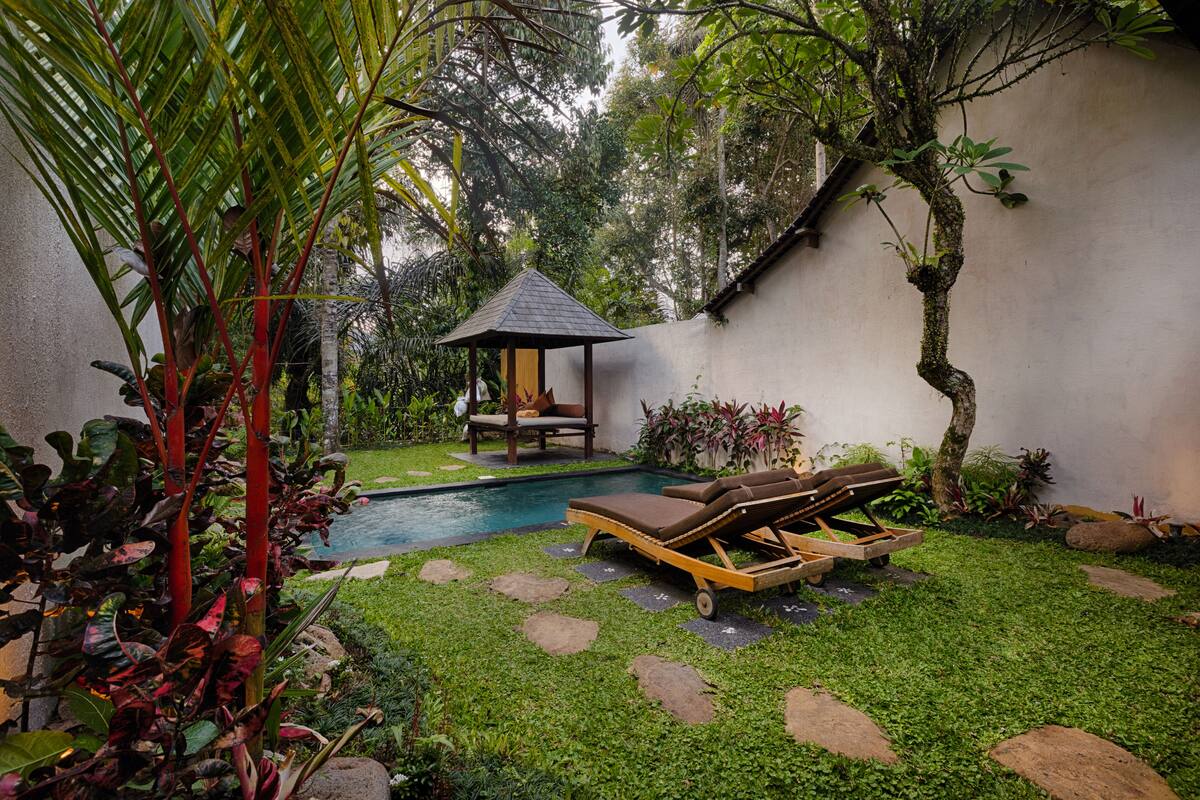 Un área de piscina privada con una tumbona, un pequeño pabellón y abundante vegetación.