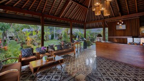 A spacious indoor area with a high ceiling, wooden beams, and a patterned floor. There are seating arrangements and a reception desk. - Ubud Padi Villas (Ubud)