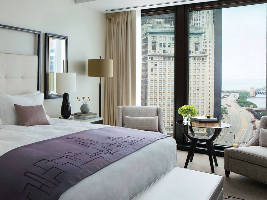 A modern hotel room with a large bed, a sitting area with a view of a cityscape.