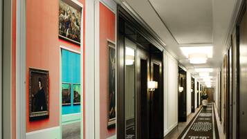 A hotel hallway with a patterned carpet, framed artwork on the walls, and a row of doors.