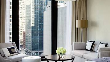 A modern hotel room with a large window offering a city view, a sofa, a small table with a vase, and a lamp.