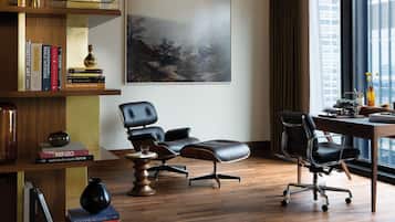 Un espace de bureau moderne avec un bureau en bois, deux chaises de bureau noires, une bibliothèque remplie de livres et un grand tableau abstrait accroché au mur.