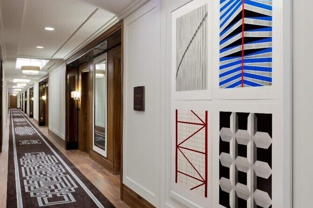 A hotel hallway with a patterned carpet, recessed lighting, and wall art.