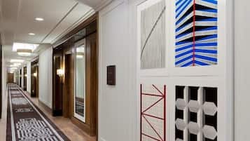 A hotel hallway with a patterned carpet, recessed lighting, and wall art.