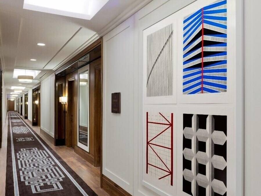 A hotel hallway with a patterned carpet, recessed lighting, and wall art.