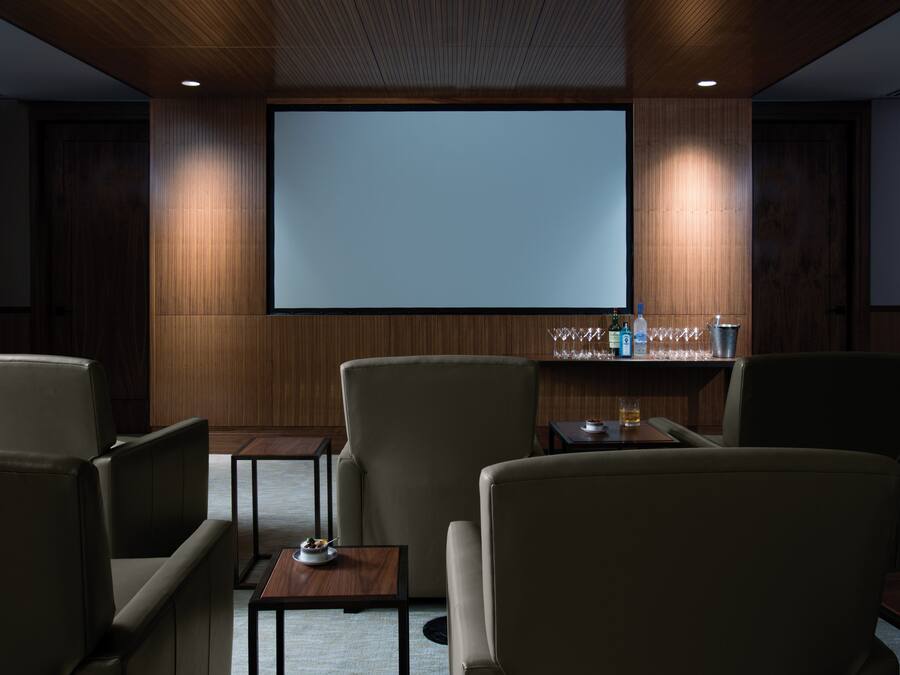 Een moderne kamer met een groot scherm, comfortabele zitplaatsen en een barhoek met glazen en flessen.