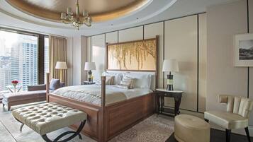 A modern hotel room with a large bed, a sitting area with a bench, a side table, and a view of the city.